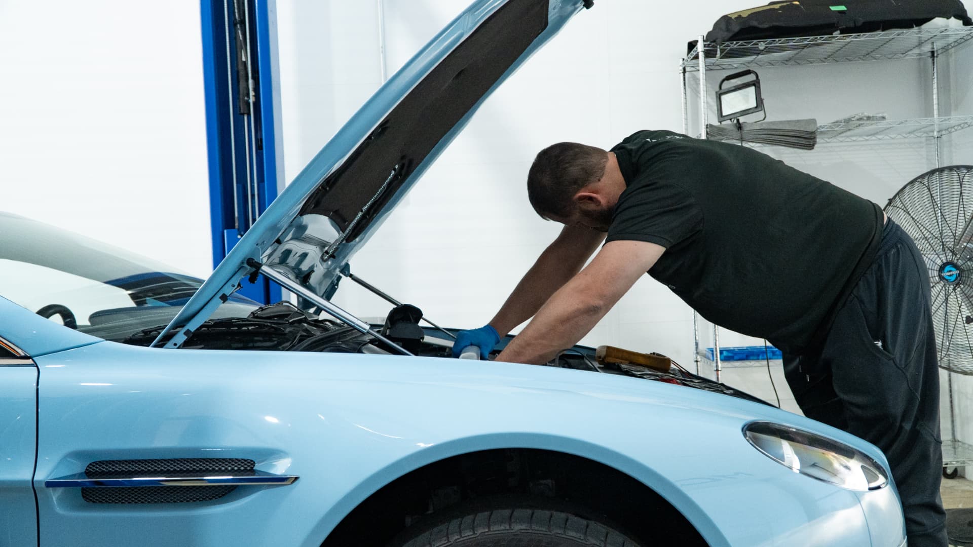 Technician servicing the V12 engine of a light blue Aston Martin DB11 at March Motorsports