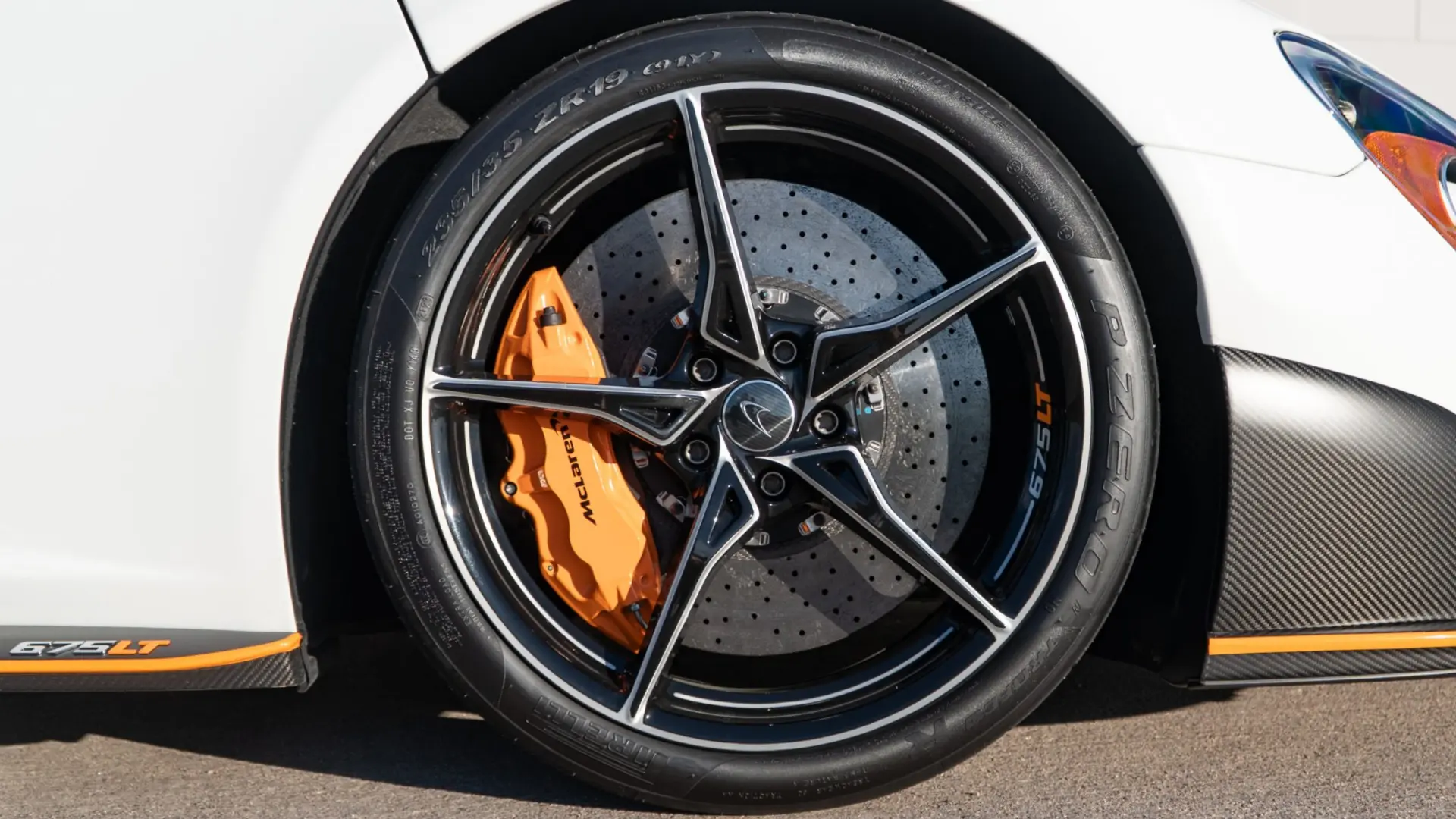 Close-up of a white McLaren 675LT wheel with an orange brake caliper and drilled carbon ceramic disc at March Motorsports