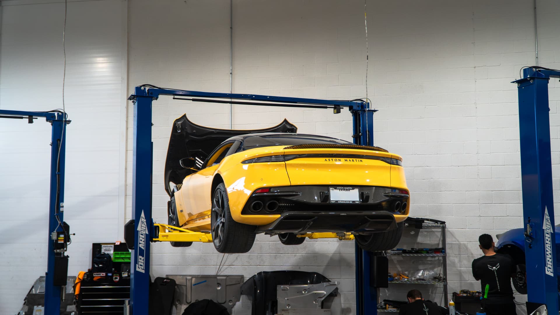 Yellow Aston Martin DBS Superleggera on the lift at March Motorsports with technicians working below