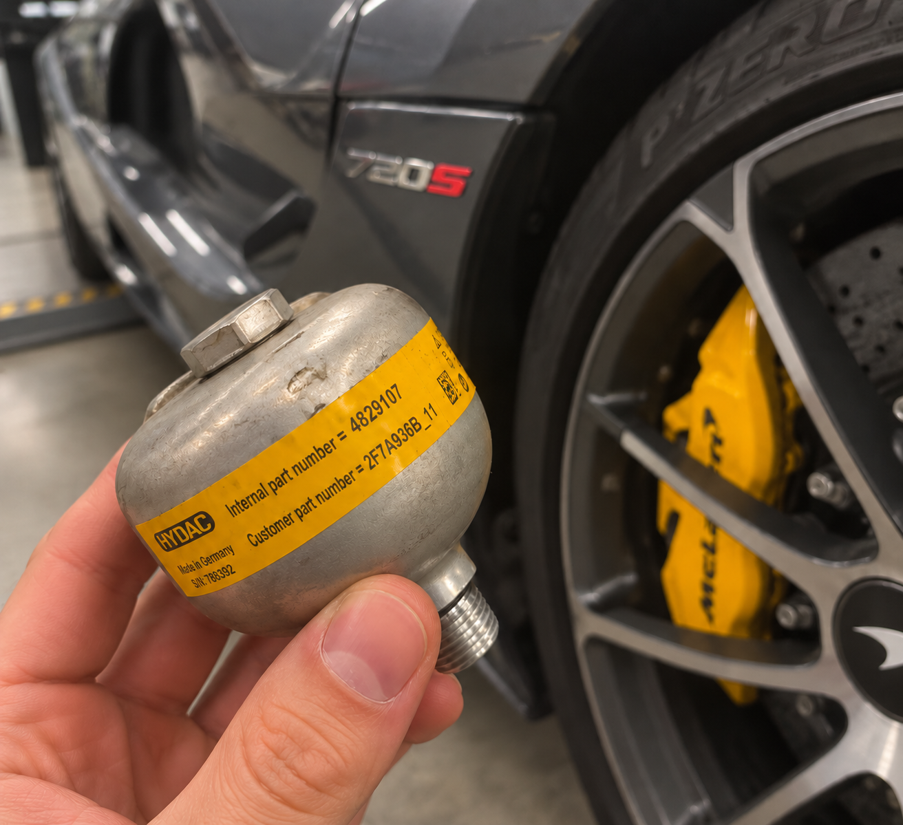 A genuine HYDAC hydraulic accumulator held in front of a McLaren 720S at March Motorsports