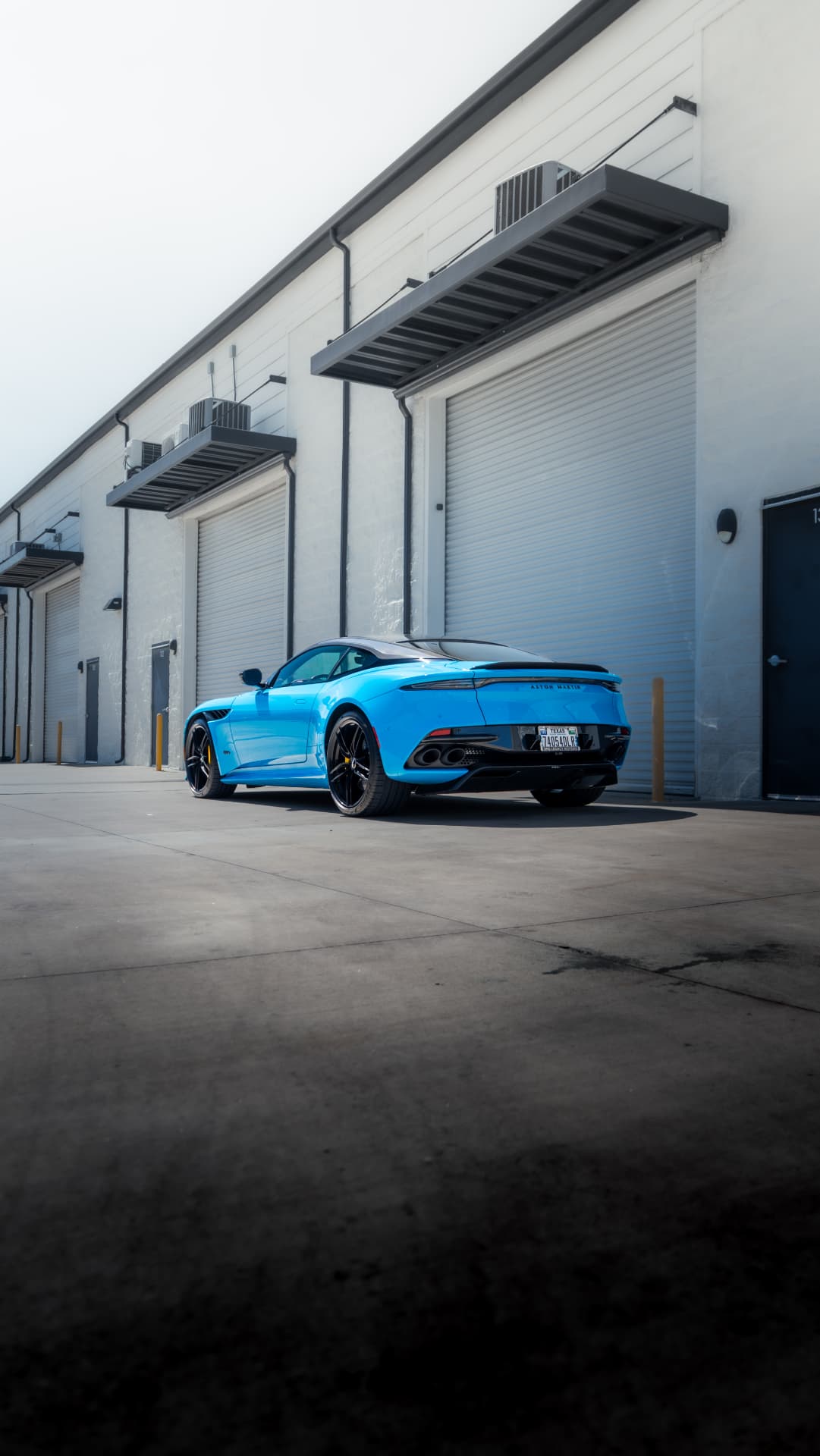 Rear three-quarter of a blue Aston Martin DBS Superleggera outside March Motorsports in Carrollton