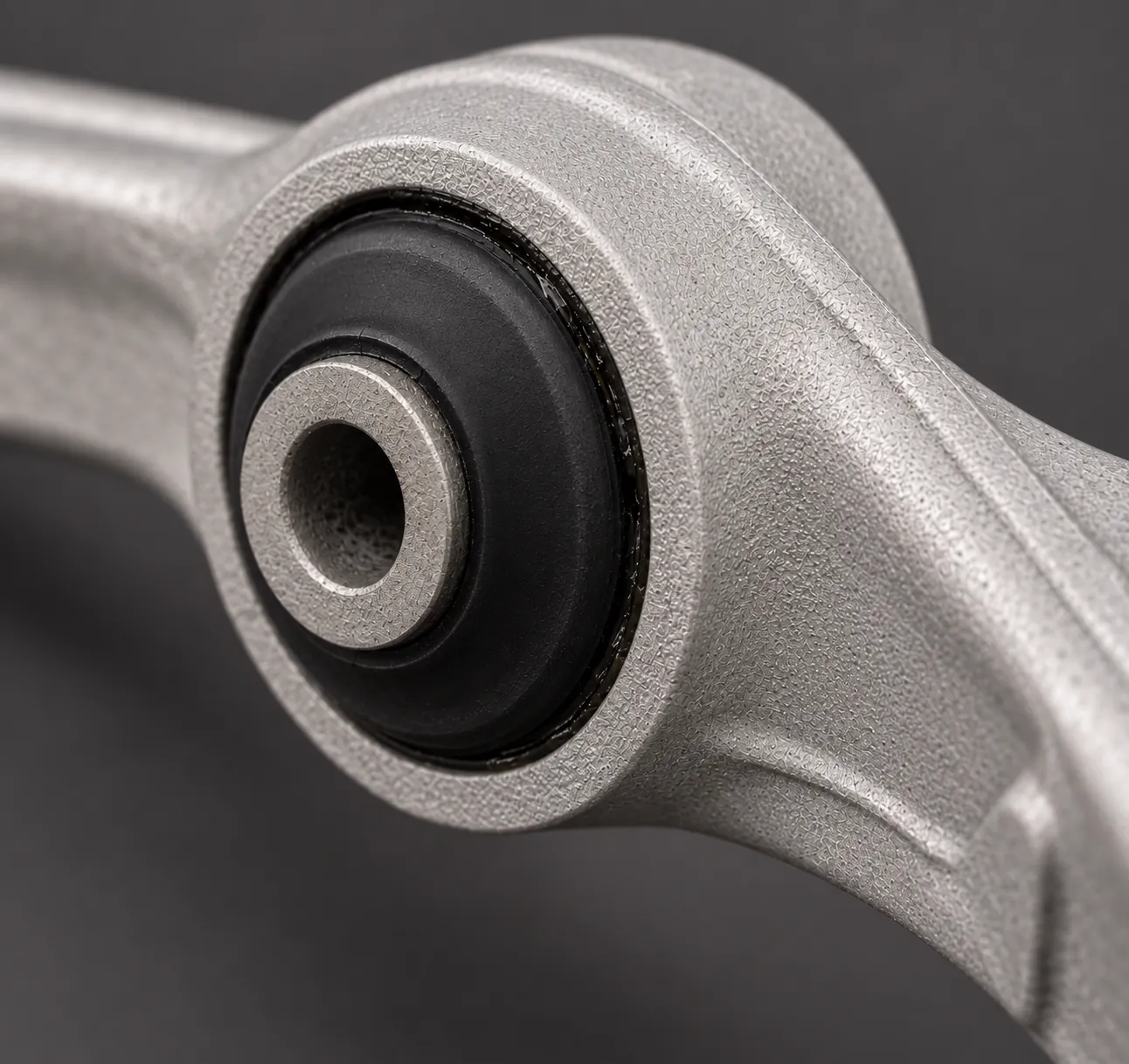 Macro shot of a cast aluminum McLaren suspension control arm at the bushing housing, black rubber bushing pressed in place