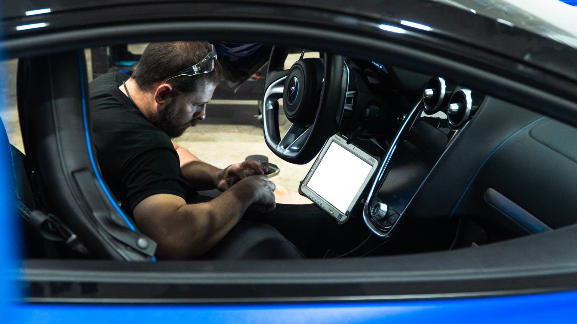 Technician running diagnostics from the driver's seat of a blue McLaren GT