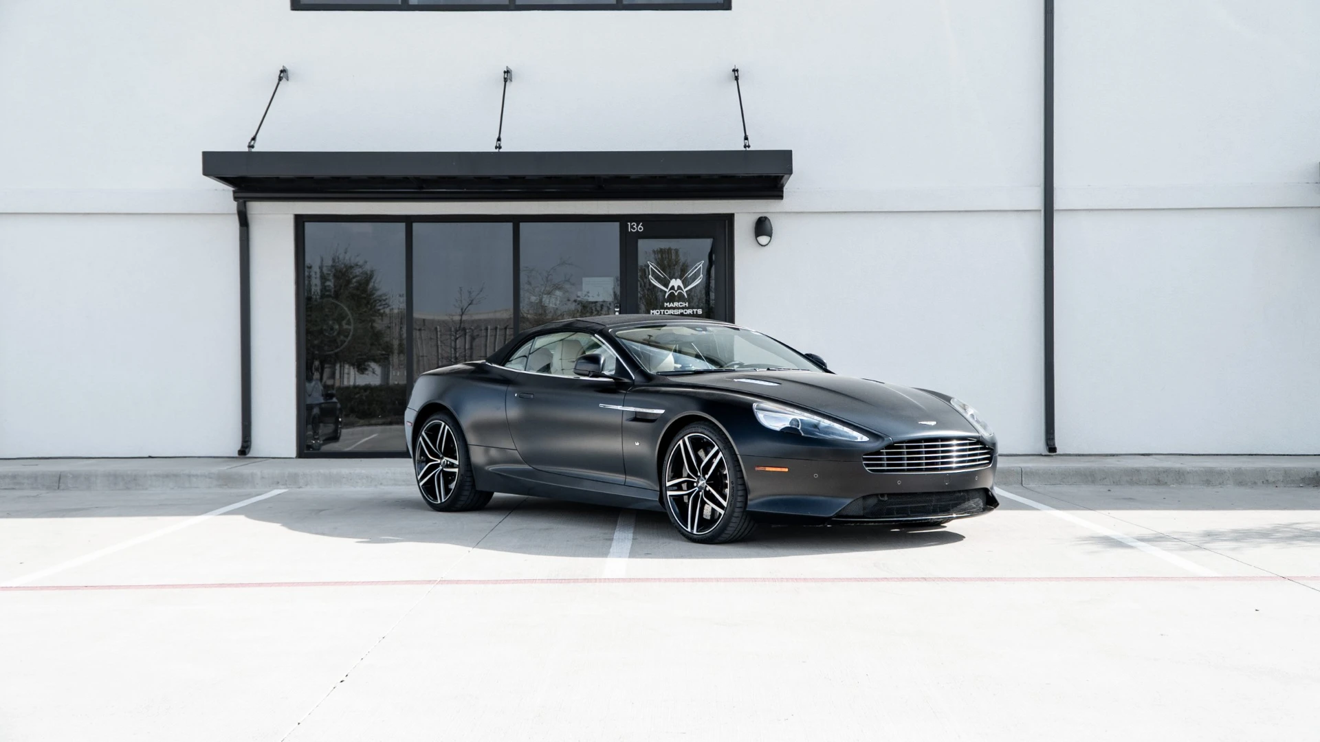 Satin black Aston Martin DB9 Volante parked in front of the March Motorsports shop in Carrollton